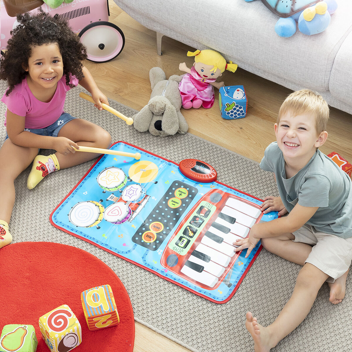 Two children playing with a musical mat on the floor surrounded by toys.