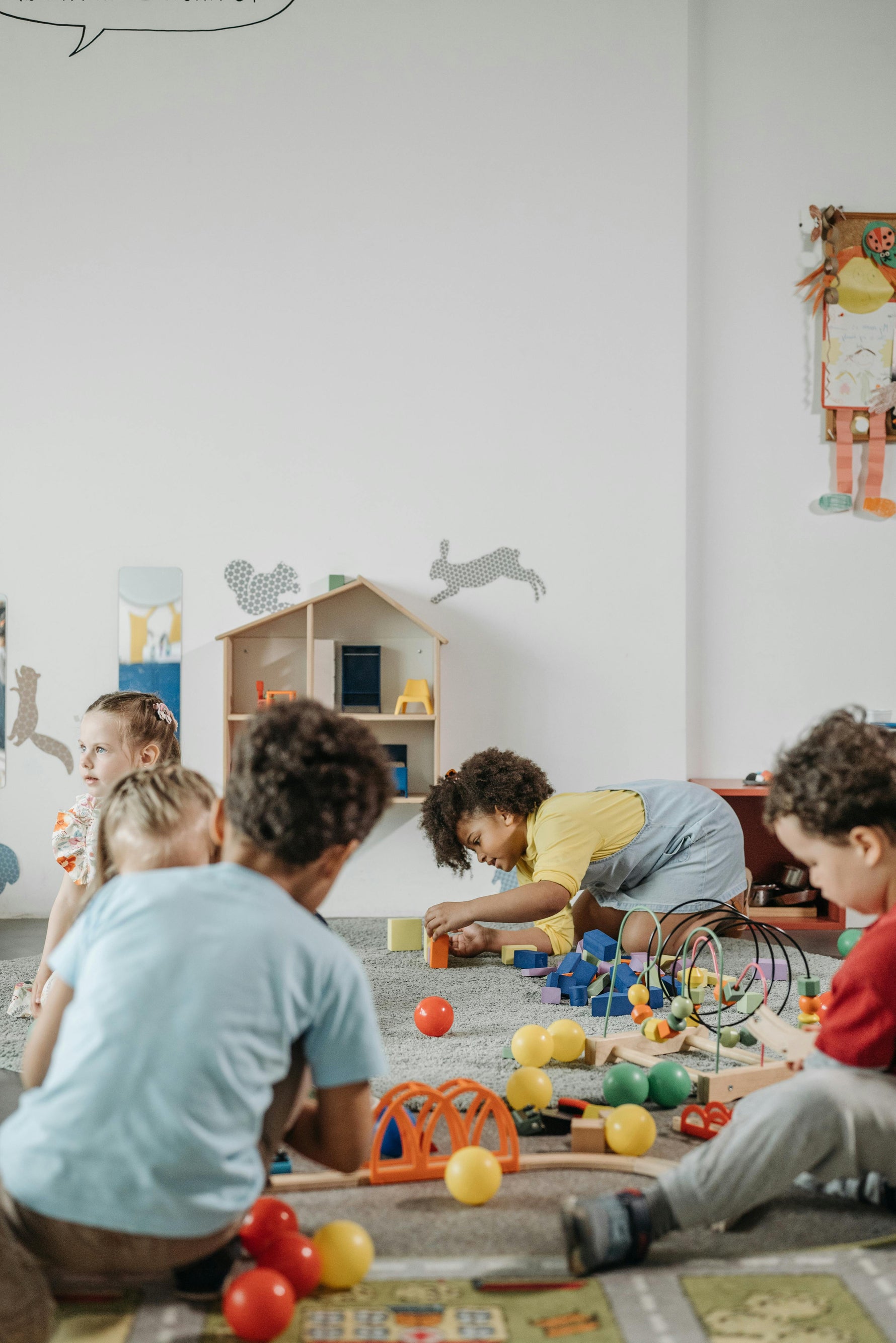 Children playing with toys on a carpeted floor in a classroom setting.